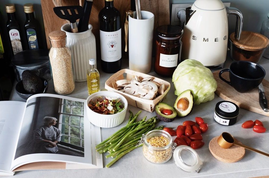 Various colorful healthy food and vegetables locating on countertop next to many different utensils and white kettle during cooking in stylish kitchen
